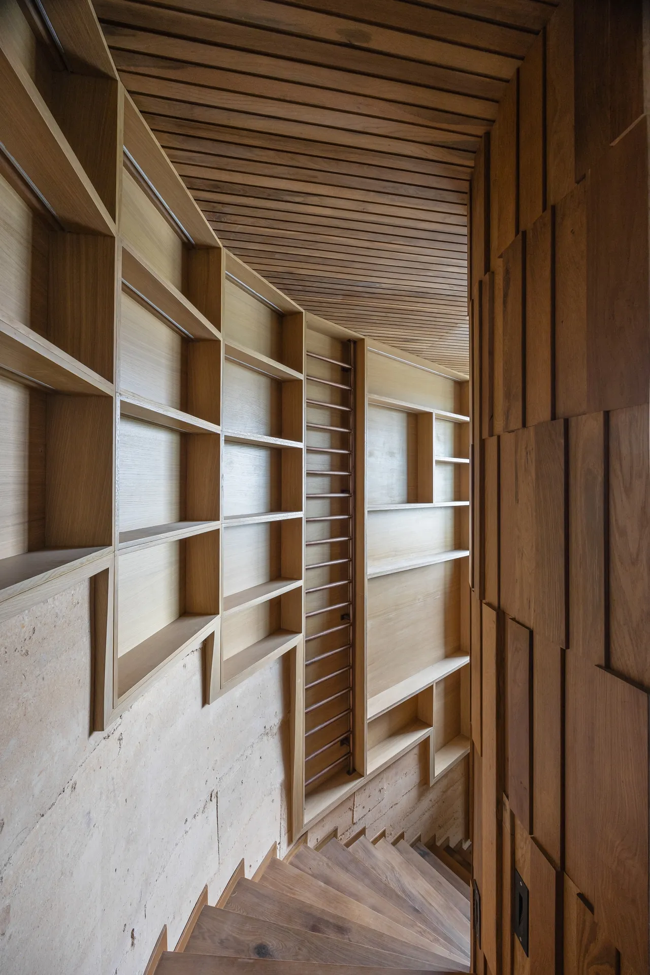 A wall shelving system built into the wall with a winding staircase leading down